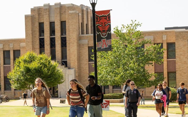 A-State students walking past Wilson Hall beneath a Red Wolves banner during the first week of the fall semester