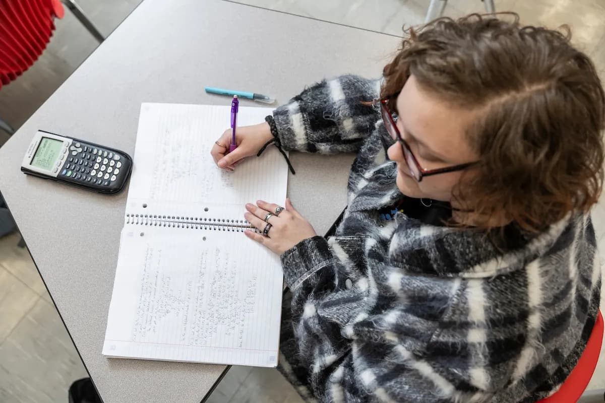 An A-State student working through math equations with a calculator and notebook