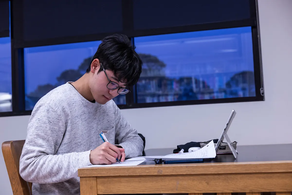 An A-State student studying with a tablet and handwritten notes in the library in the evening