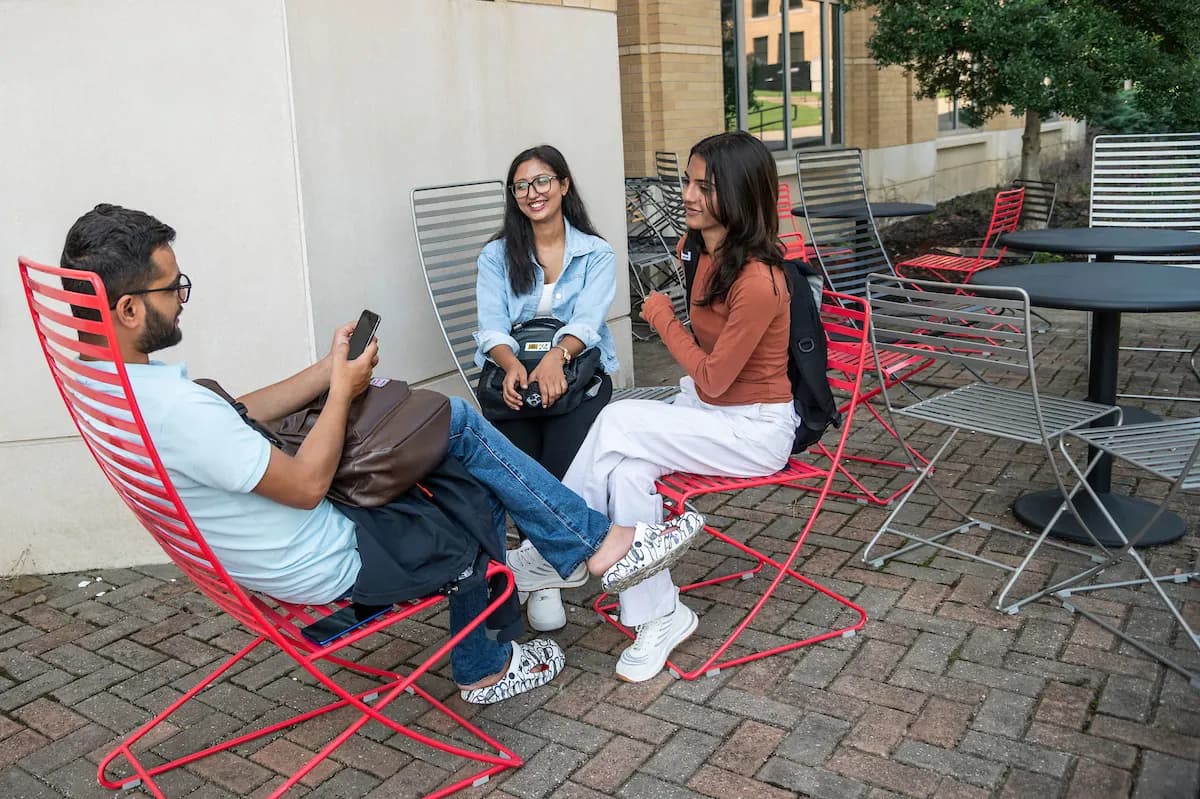 A-State students sitting and talking on red chairs on a campus patio