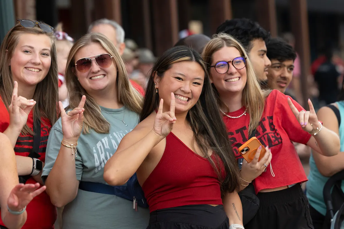A-State students smiling and making the Red Wolves hand sign