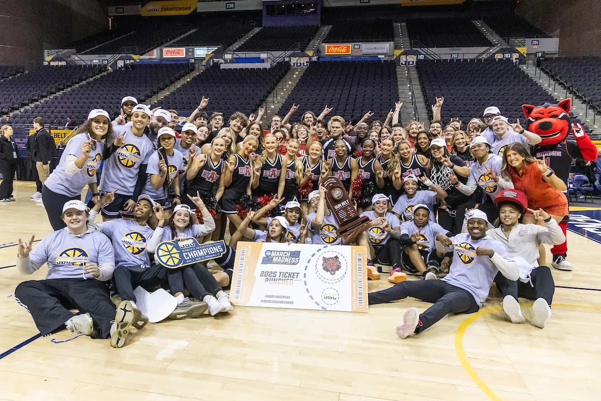 A-State athletes celebrating with a championship trophy on the basketball court