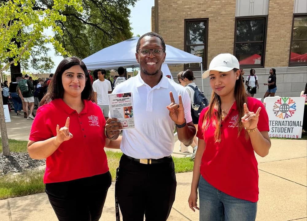 Three Center for Leadership Excellence members giving the Wolves Up hand sign at an event