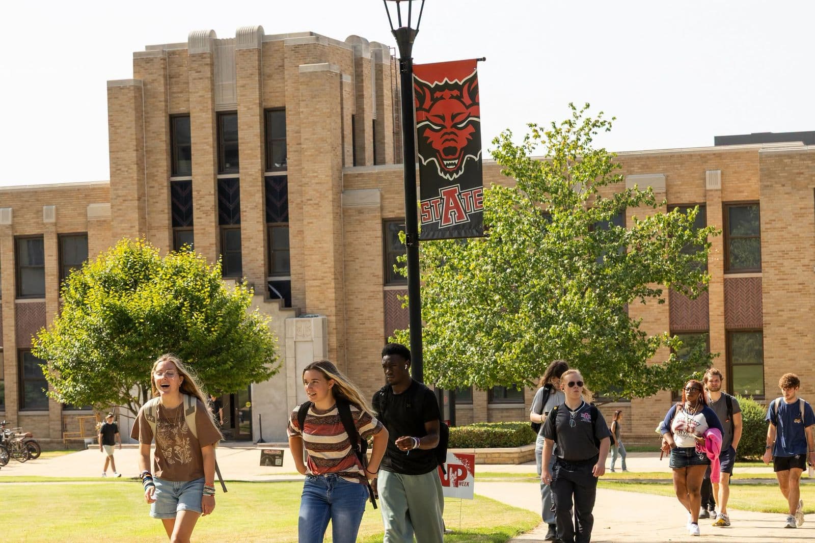 A-State students walking past Wilson Hall beneath a Red Wolves banner during the first week of the fall semester